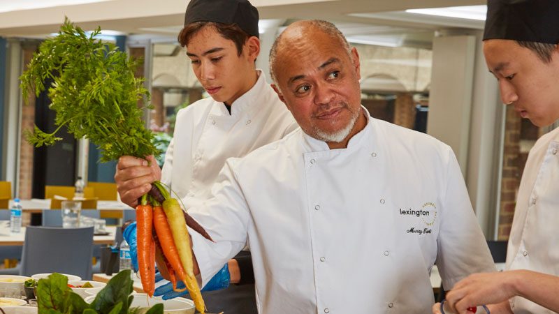 Chef holding up carrots with cooks in the kitchen
